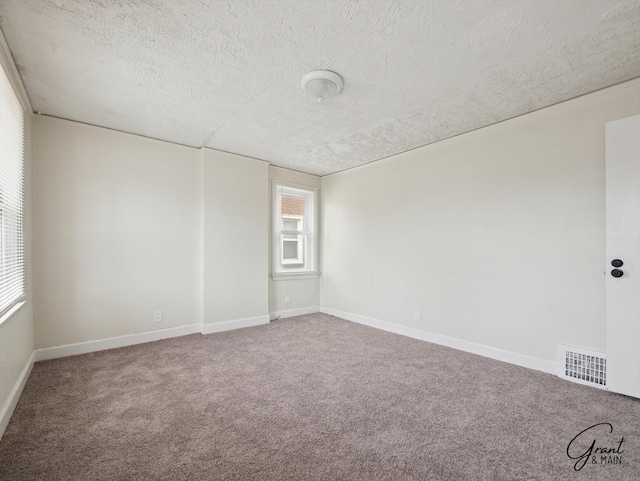 carpeted spare room with a textured ceiling, visible vents, and baseboards