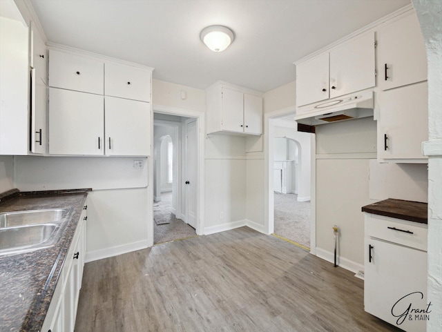 kitchen featuring dark countertops, under cabinet range hood, light wood-style floors, white cabinetry, and a sink