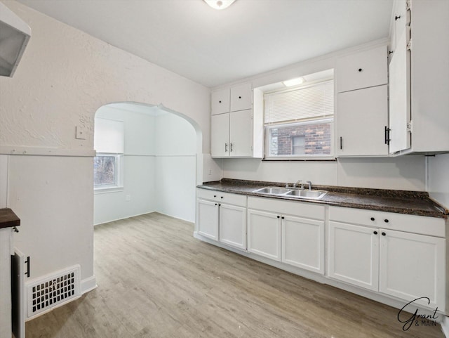 kitchen with dark countertops, visible vents, light wood-style flooring, white cabinetry, and a sink