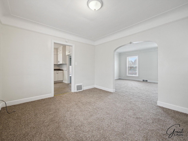 carpeted spare room with visible vents, arched walkways, and baseboards