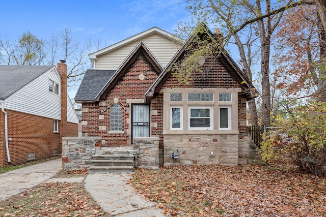 view of front facade featuring stone siding, brick siding, roof with shingles, and fence