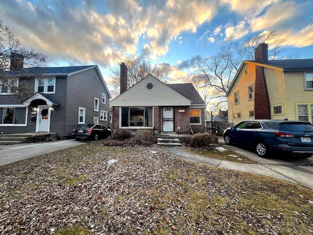 bungalow featuring driveway, a chimney, and brick siding