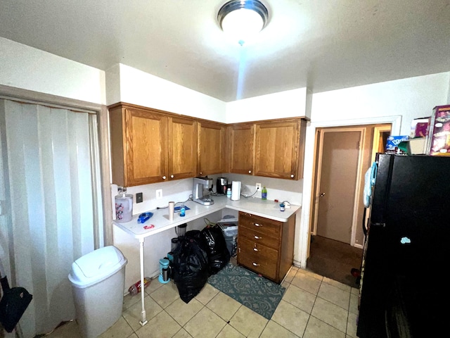 kitchen with light tile patterned floors, light countertops, brown cabinetry, and freestanding refrigerator