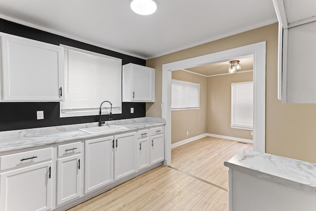 kitchen featuring baseboards, white cabinets, light stone counters, light wood-type flooring, and a sink