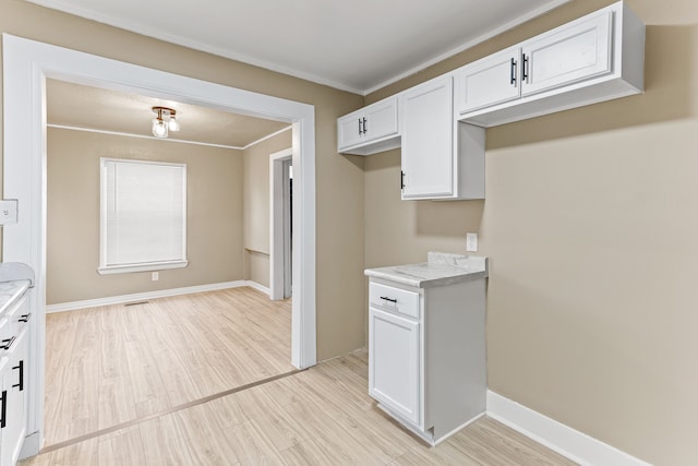 kitchen with baseboards, white cabinets, light countertops, ornamental molding, and light wood-style floors