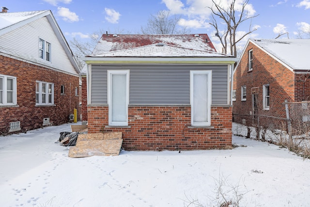 snow covered house featuring brick siding and fence