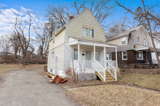 view of front of house featuring aphalt driveway, a porch, and a chimney