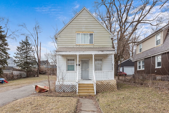 shotgun-style home with covered porch, a detached garage, roof with shingles, and fence