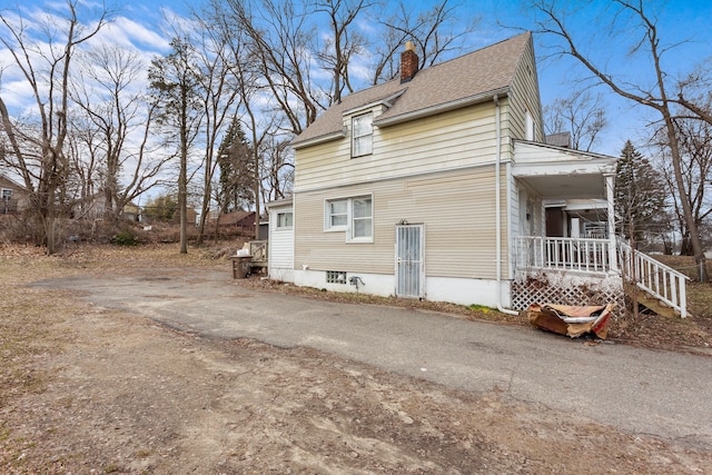 view of side of home featuring a porch, a chimney, driveway, and roof with shingles