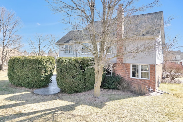 view of side of home featuring brick siding, a yard, a chimney, and roof with shingles