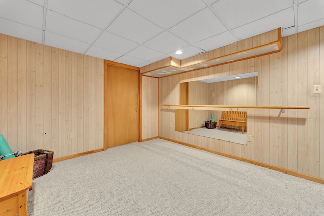 finished below grade area featuring baseboards, a paneled ceiling, carpet, and wooden walls