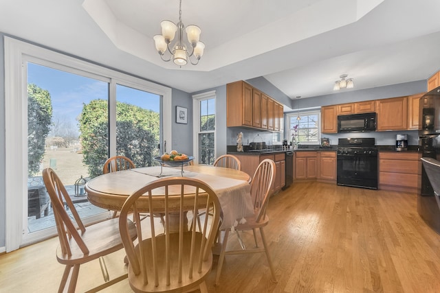 dining space with a raised ceiling, a notable chandelier, and light wood-type flooring