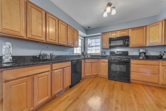 kitchen with visible vents, dark stone counters, light wood-type flooring, black appliances, and a sink