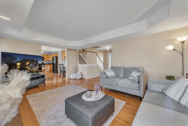 living room featuring stairway, light wood-style flooring, baseboards, and a tray ceiling