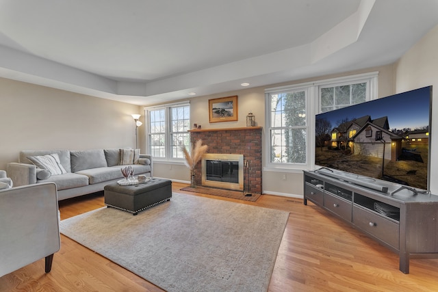 living room featuring light wood-style flooring, a brick fireplace, and baseboards