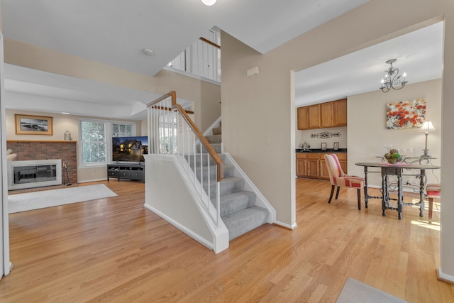 staircase featuring baseboards, a notable chandelier, a brick fireplace, and wood finished floors