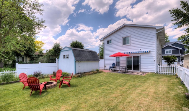 back of property featuring a fire pit, a lawn, a fenced backyard, a storage unit, and an outdoor structure