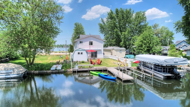 dock area with a lawn, a water view, boat lift, and fence