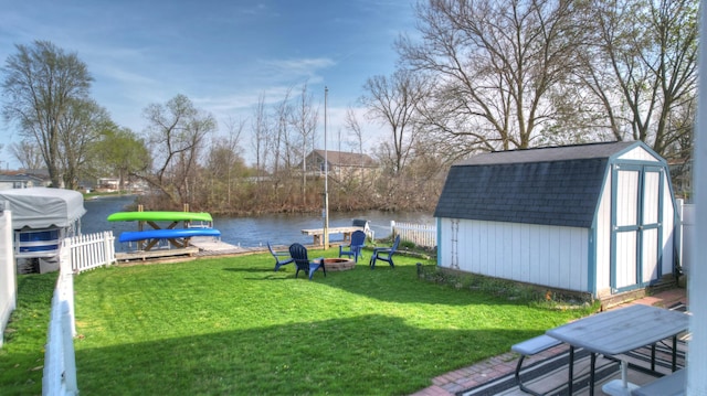 view of yard with a water view, fence, a shed, an outdoor structure, and a fire pit