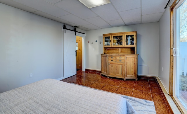 unfurnished bedroom featuring a barn door, visible vents, baseboards, dark tile patterned flooring, and a paneled ceiling