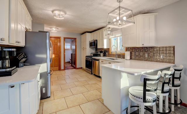 kitchen with tasteful backsplash, appliances with stainless steel finishes, a peninsula, light countertops, and a sink