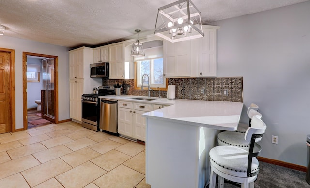 kitchen with a peninsula, a sink, a kitchen breakfast bar, appliances with stainless steel finishes, and tasteful backsplash