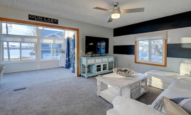 carpeted living area with a ceiling fan, visible vents, and a textured ceiling