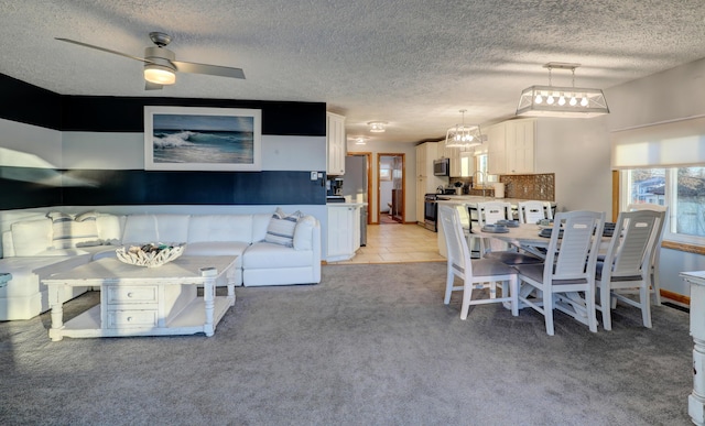 living area with light carpet, ceiling fan, and a textured ceiling