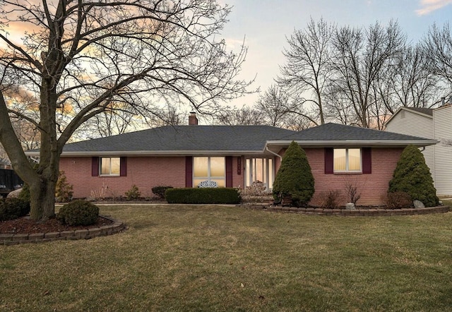 single story home with roof with shingles, brick siding, a chimney, and a front yard