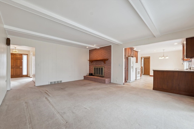 unfurnished living room featuring a brick fireplace, visible vents, beamed ceiling, and light colored carpet