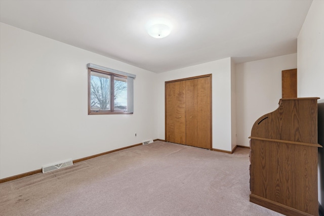 unfurnished bedroom featuring light carpet, a closet, visible vents, and baseboards