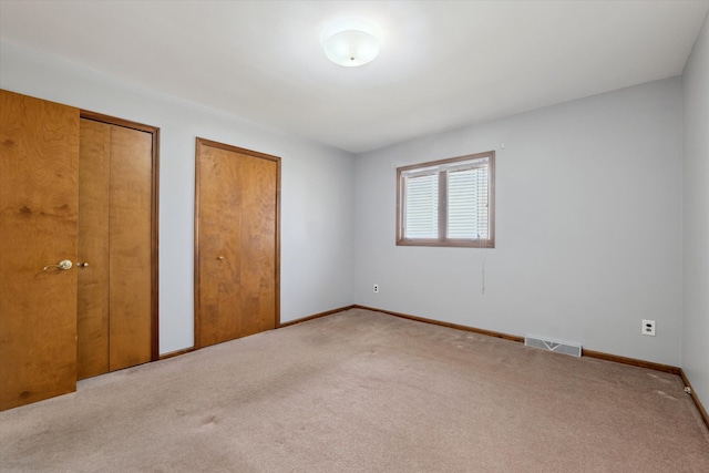 unfurnished bedroom featuring baseboards, carpet flooring, visible vents, and multiple closets