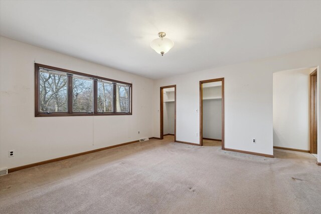 unfurnished bedroom featuring light carpet, baseboards, visible vents, and multiple closets