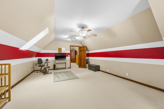 interior space with carpet floors, vaulted ceiling with skylight, a ceiling fan, and baseboards