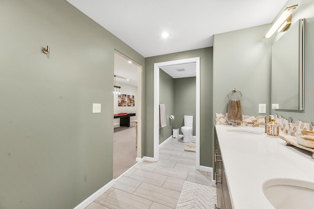 full bathroom featuring toilet, double vanity, baseboards, and a sink