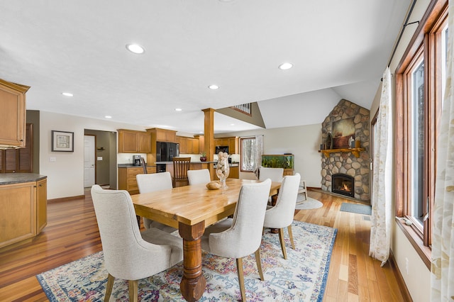 dining space with light wood finished floors, baseboards, vaulted ceiling, a stone fireplace, and recessed lighting