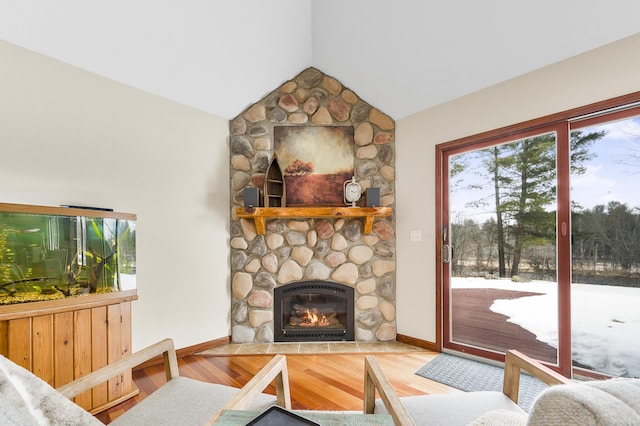 living area featuring vaulted ceiling, a stone fireplace, wood finished floors, and baseboards