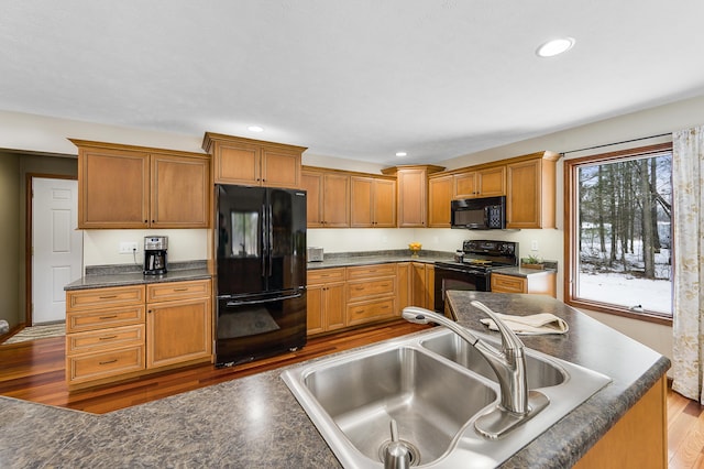 kitchen featuring recessed lighting, wood finished floors, a sink, black appliances, and dark countertops