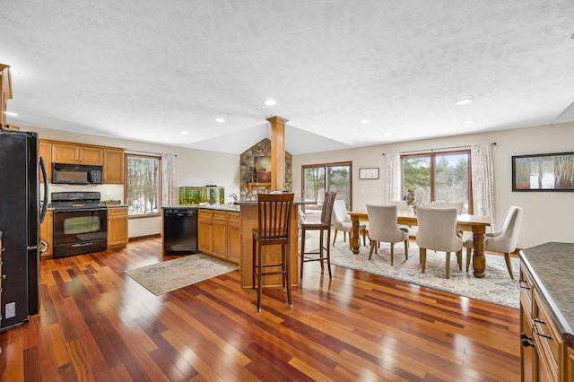 kitchen with black appliances, plenty of natural light, brown cabinets, and hardwood / wood-style flooring