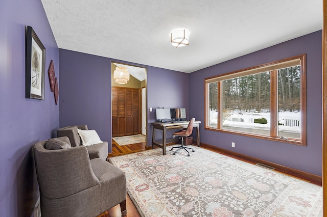 office space with visible vents, a textured ceiling, baseboards, and wood finished floors