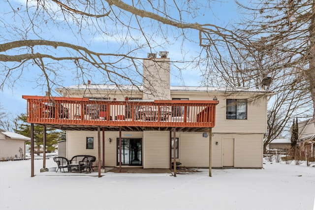 snow covered rear of property featuring a chimney and a wooden deck