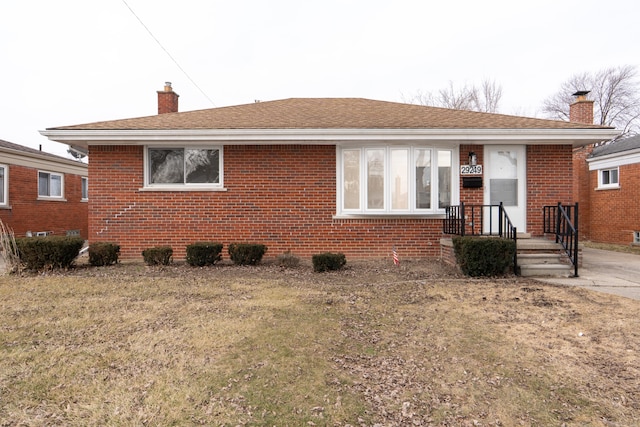 view of front facade with roof with shingles, brick siding, and a chimney