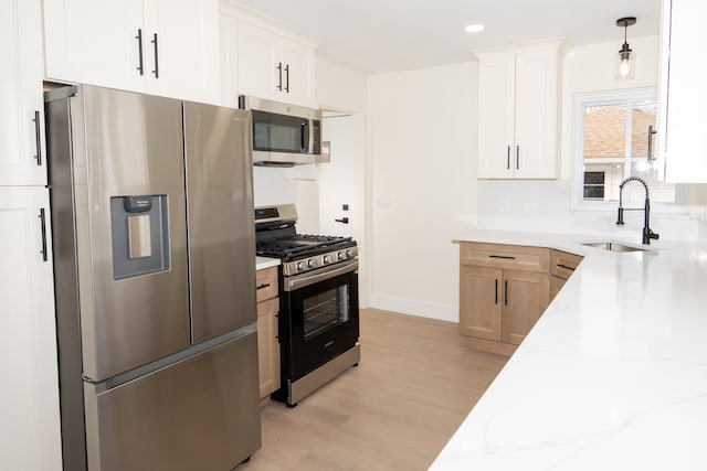 kitchen with light stone counters, a sink, white cabinetry, appliances with stainless steel finishes, and light wood finished floors