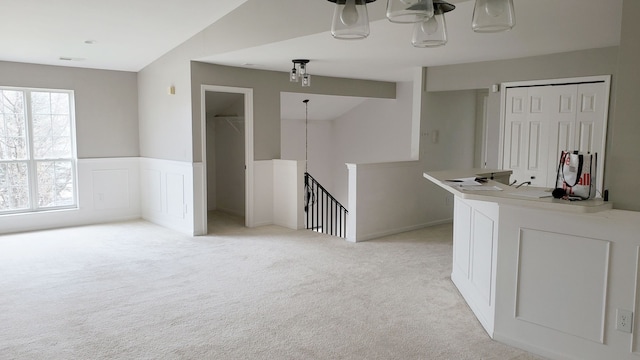 spare room featuring lofted ceiling, a decorative wall, light colored carpet, and a wainscoted wall