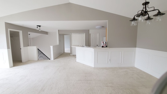 empty room with a decorative wall, light colored carpet, wainscoting, and vaulted ceiling