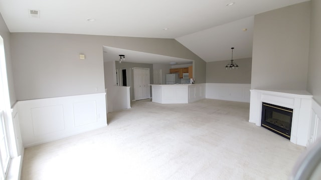 unfurnished living room with a decorative wall, a wainscoted wall, vaulted ceiling, light carpet, and a glass covered fireplace