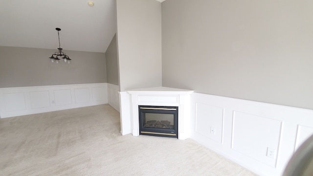 interior details featuring a glass covered fireplace, carpet flooring, wainscoting, an inviting chandelier, and a decorative wall