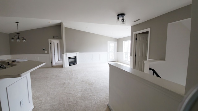 interior space with vaulted ceiling, a glass covered fireplace, light colored carpet, and a wainscoted wall