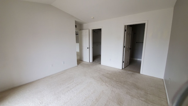 unfurnished bedroom featuring a walk in closet, light colored carpet, lofted ceiling, a closet, and ensuite bath