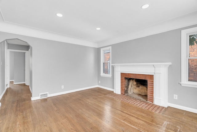 unfurnished living room featuring arched walkways, a brick fireplace, visible vents, and baseboards